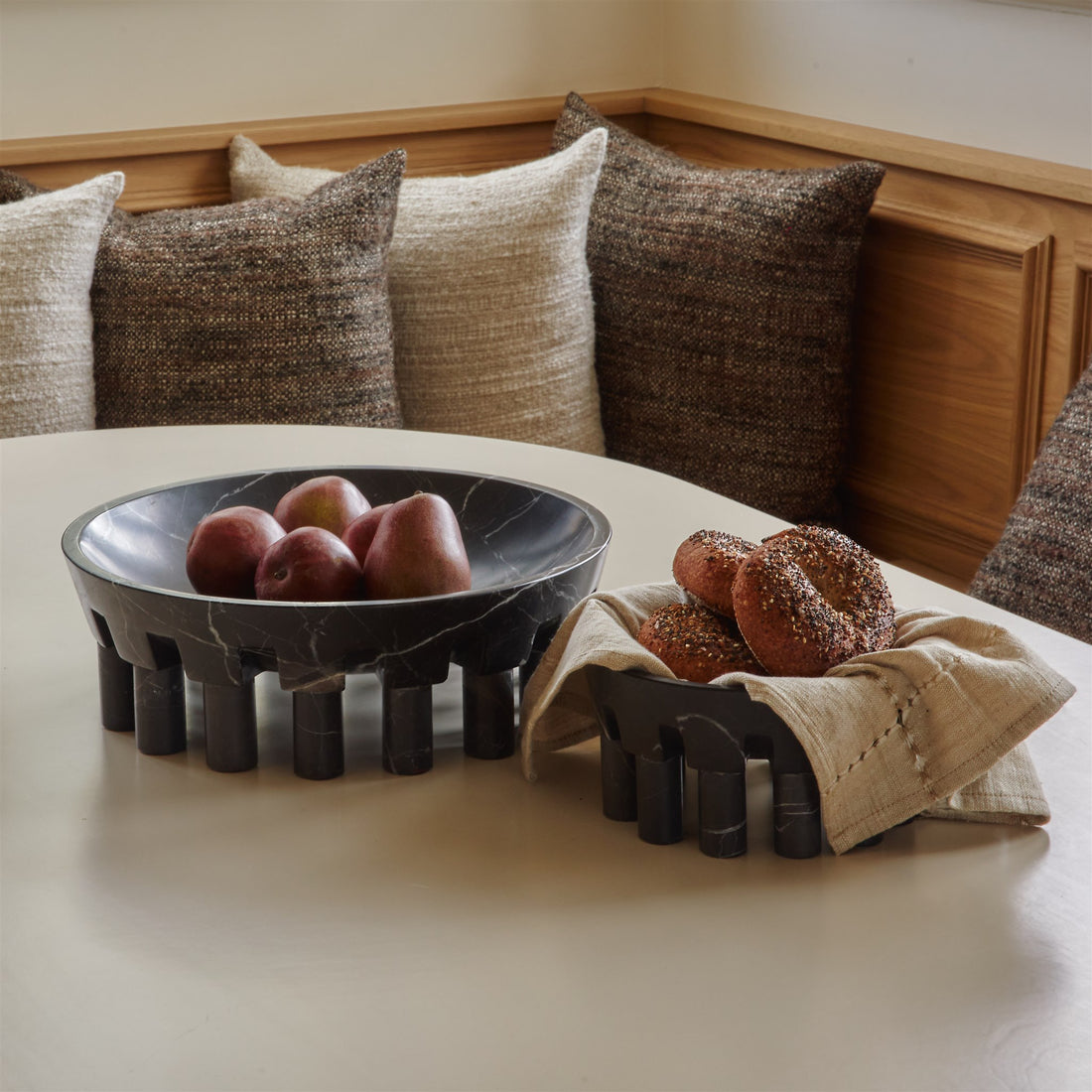 Two bowls made from black marble in a breakfast nook holding fresh bagels and apples.